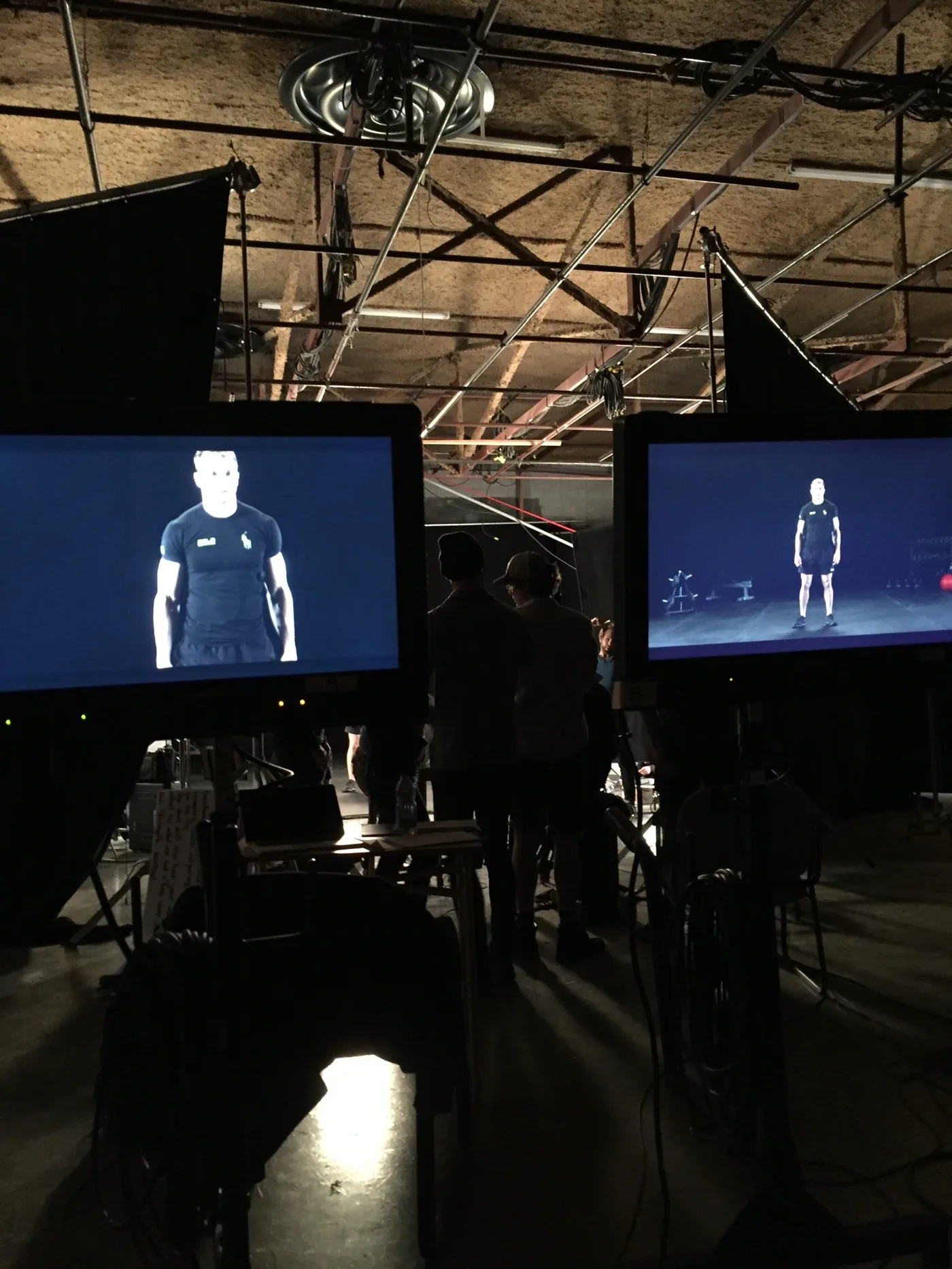 Behind the scenes at the PoloTech adaptive workout shoot: two monitors showing the trainer in the Polo Tech shirt, crew in silhouette